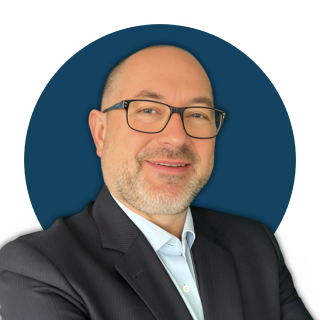 Homme souriant en costume, lunettes, avec un fond bleu circulaire.